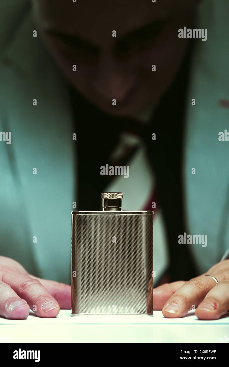 Man somberly contemplates a flask, symbolizing his struggle with alcohol addiction and its recognized health risks Stock Photo