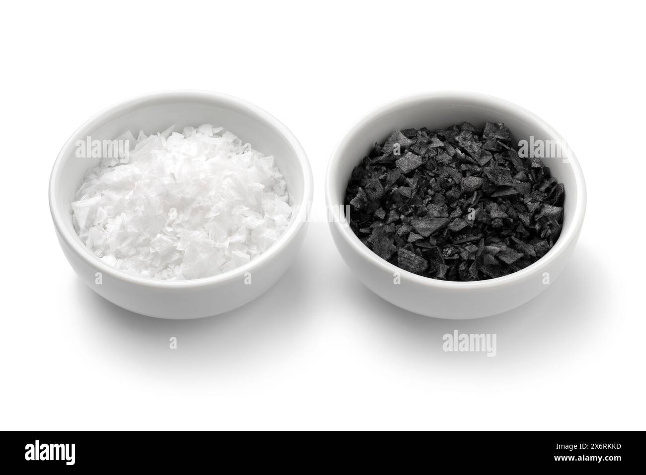 Pair of bowls with black and white sea salt flakes close up isolated on white background Stock Photo