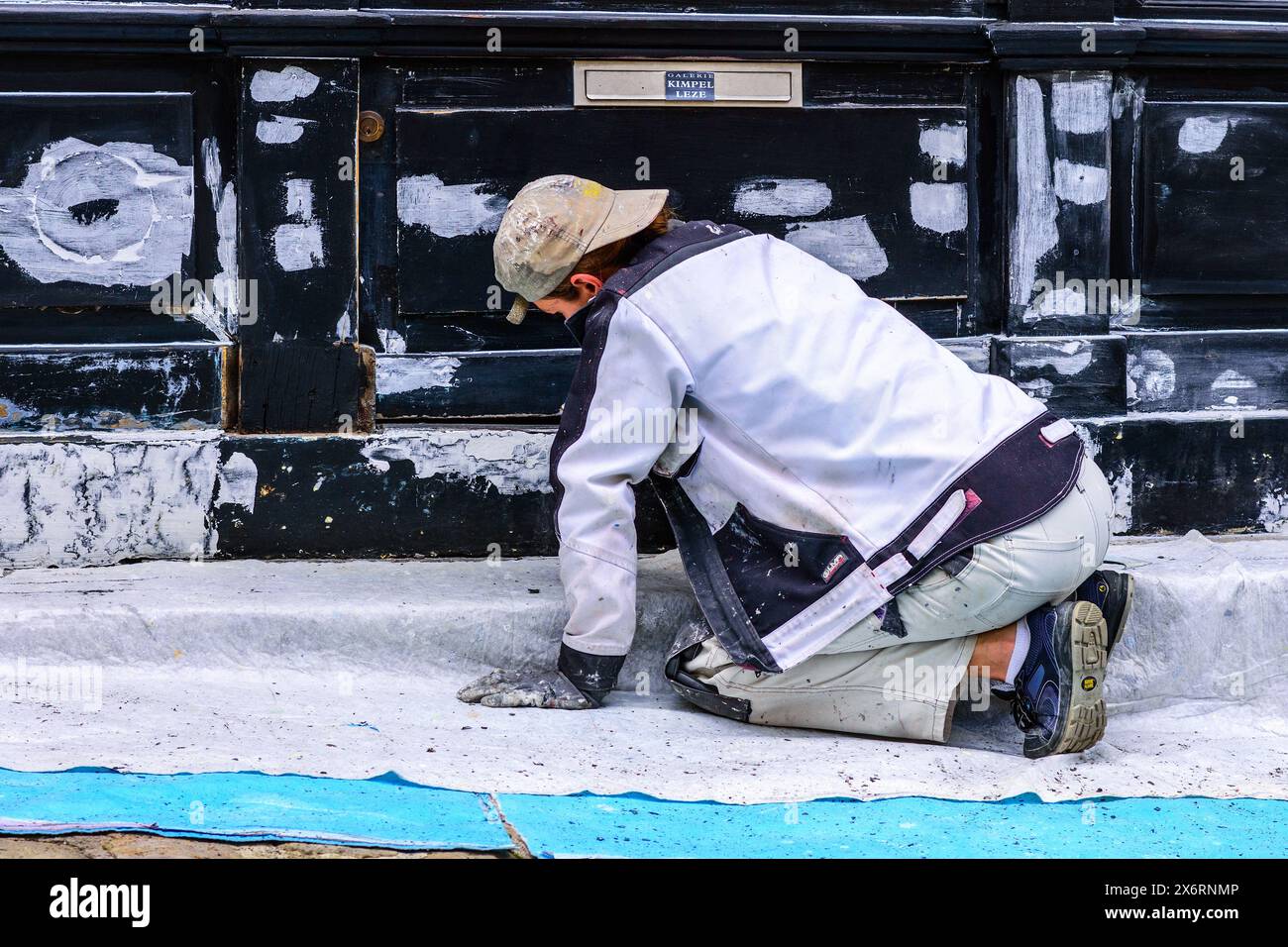 Young female decorator sanding shop front prior to repainting - Loches, Indre-et-Loire (37), France. Stock Photo