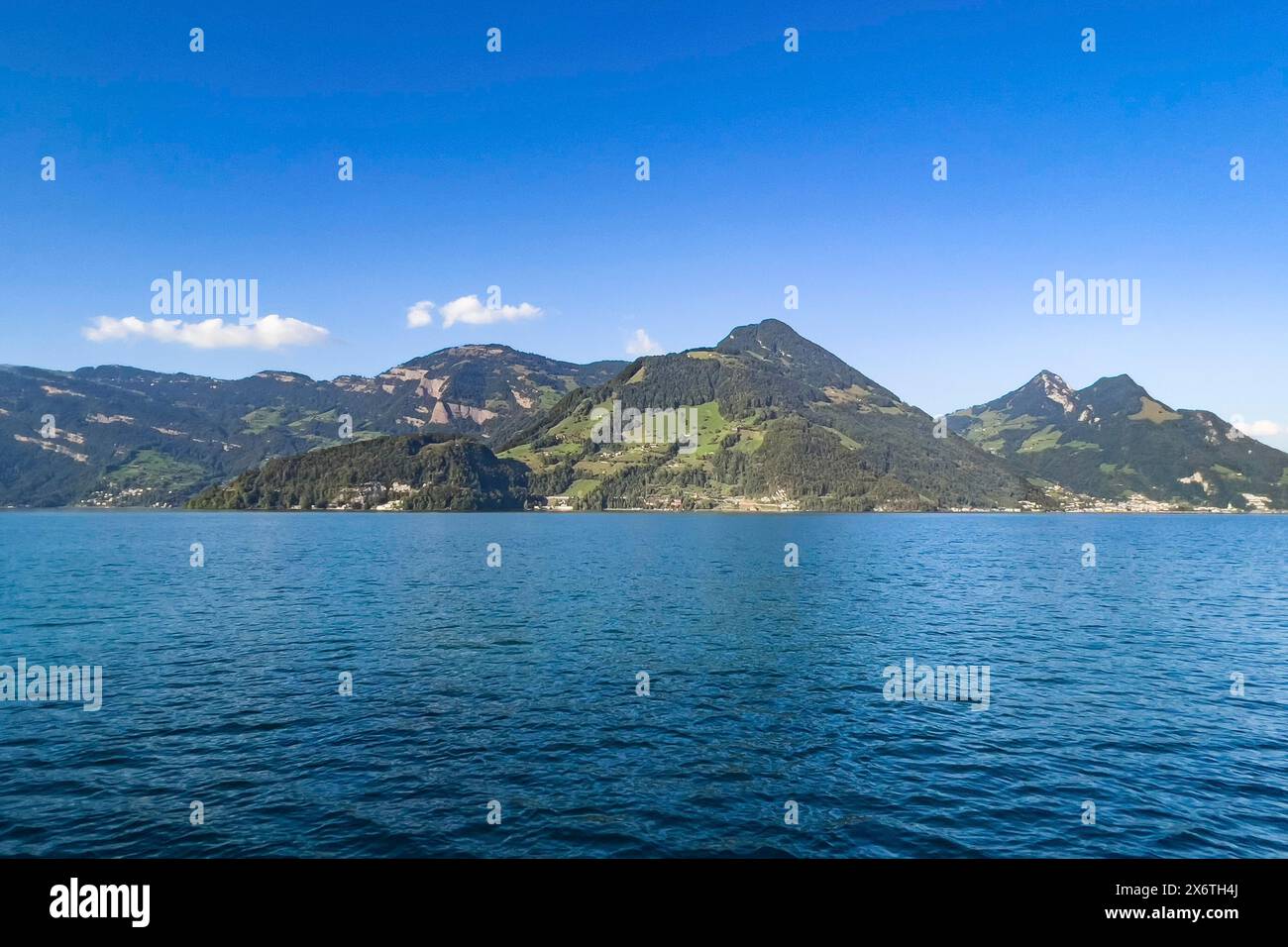 Calm lake under a clear blue sky with picturesque mountains in the background, Beckenried, Nidwalden, Switzerland Stock Photo