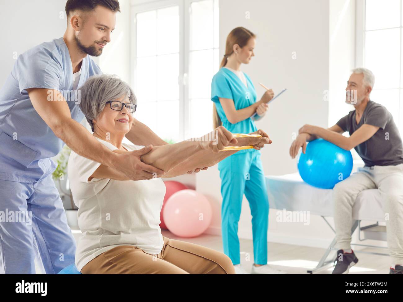 Nurse helping senior smiling woman to do sport stretching exercises with rubber band Stock Photo