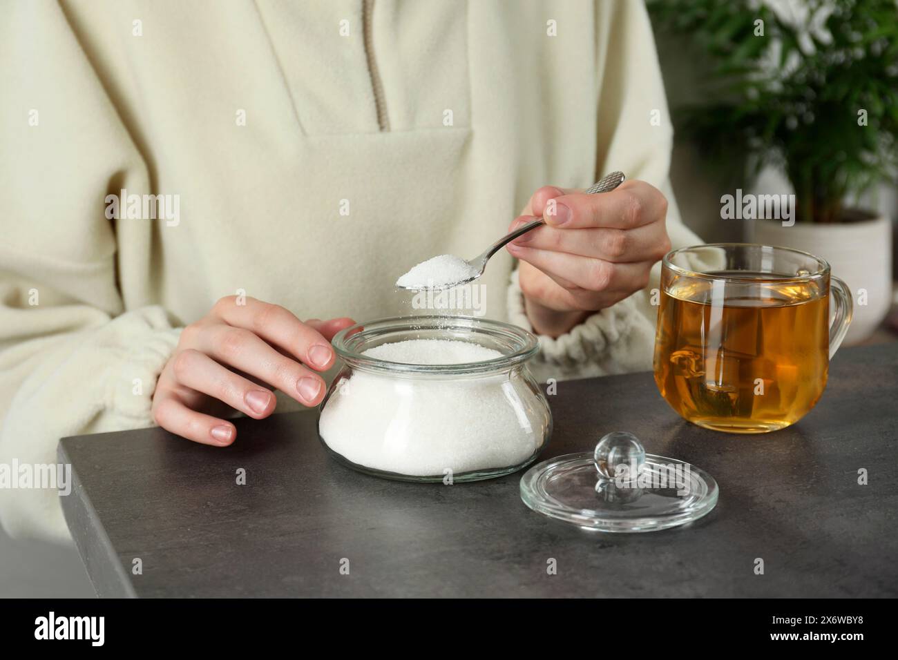 Woman adding sugar into aromatic tea at grey table indoors, closeup ...