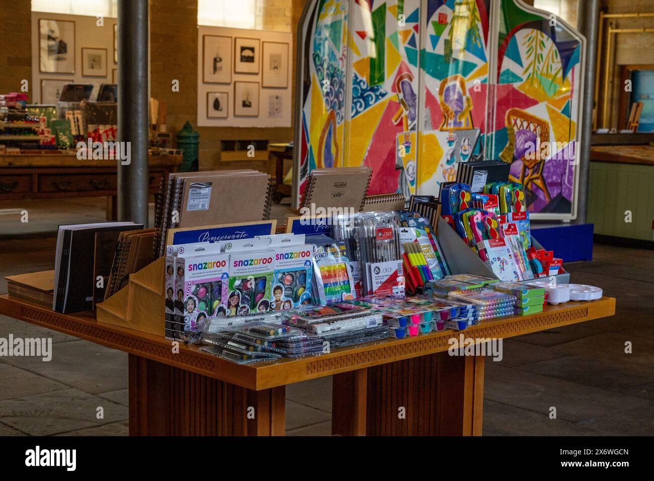 Children's art materials on a table in Salts Mill in Saltaire, Yorkshire. David Hockney art (Lithograph - 'Caribbean Teatime') is in the background. Stock Photo
