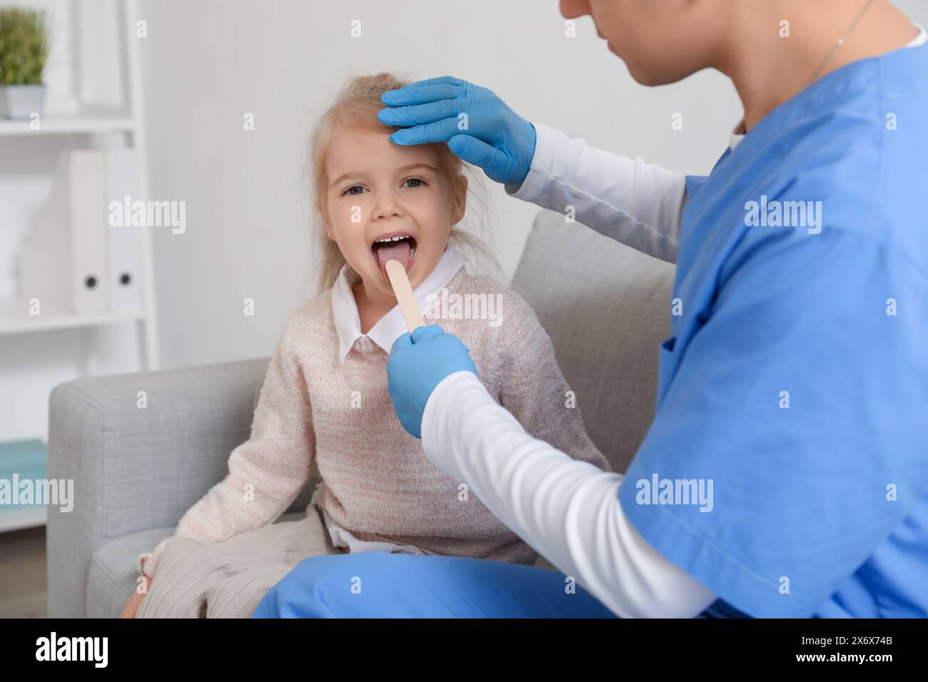 Male pediatrician examining little girl with tongue depressor in clinic