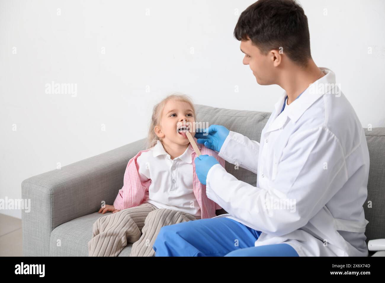 Male pediatrician examining little girl with tongue depressor in clinic