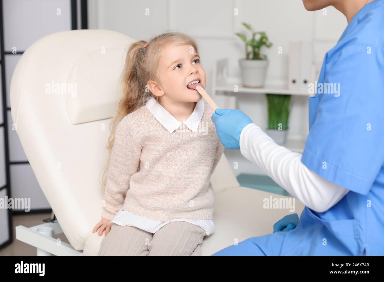 Male pediatrician examining little girl with tongue depressor in clinic