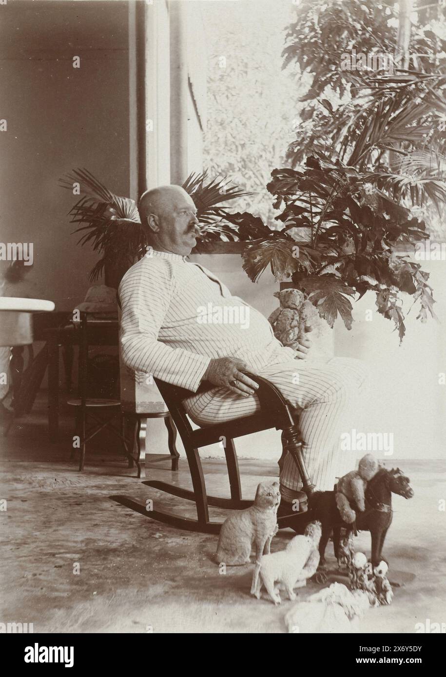 Man in his pajamas in the rocking chair on the veranda surrounded by toy animals., Banjoewangi 1910 (title on object), Photographies (series title), The men wear white tropical uniforms, one man with a pith helmet, two other men wear a straw hat, the women wear white dresses or batik skirts with white vests. Photo from album 'Photographies'., photograph, Frits Freerks Fontein Fz., (attributed to), Frits Freerks Fontein Fz., (attributed to), Madura, (possibly), Netherlands, (possibly), c. 1910, cardboard, height, 57 mm × width, 128 mm, height, 242 mm × width, 333 mm Stock Photo