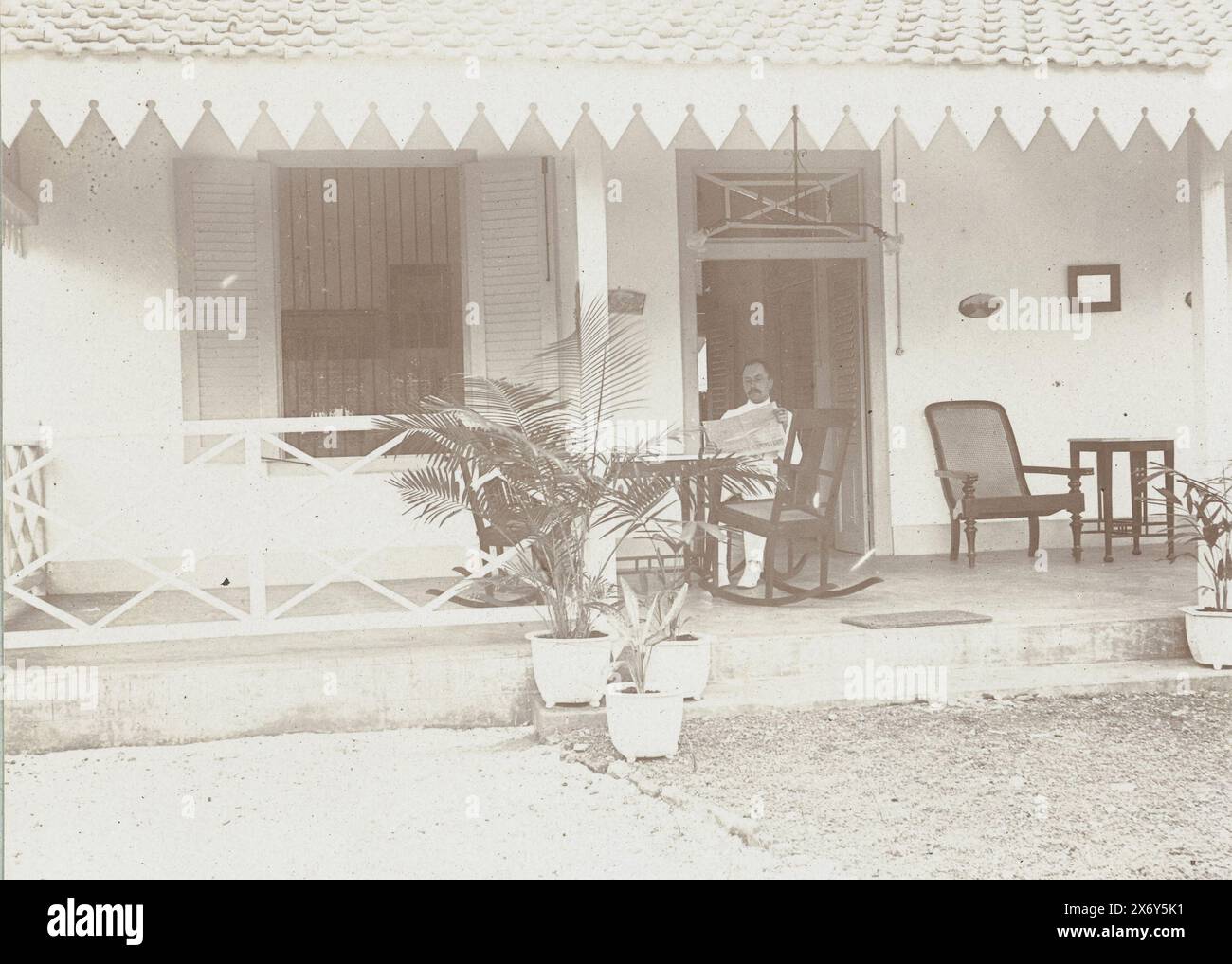 Man in a rocking chair on the veranda of a house., Kaliangel Madoera, August 2. 1910 (title on object), Photographies (series title), Photo from album 'Photographies'., photograph, Frits Freerks Fontein Fz., (attributed to), Frits Freerks Fontein Fz., (attributed to), Madura, (possibly), Netherlands, (possibly), c. 1903, cardboard, height, 79 mm × width, 109 mm, height, 242 mm × width, 333 mm Stock Photo