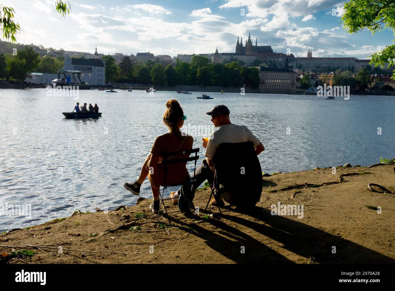 A young couple on the bank of the Vltava River enjoying the sunset Prague Castle Stock Photo