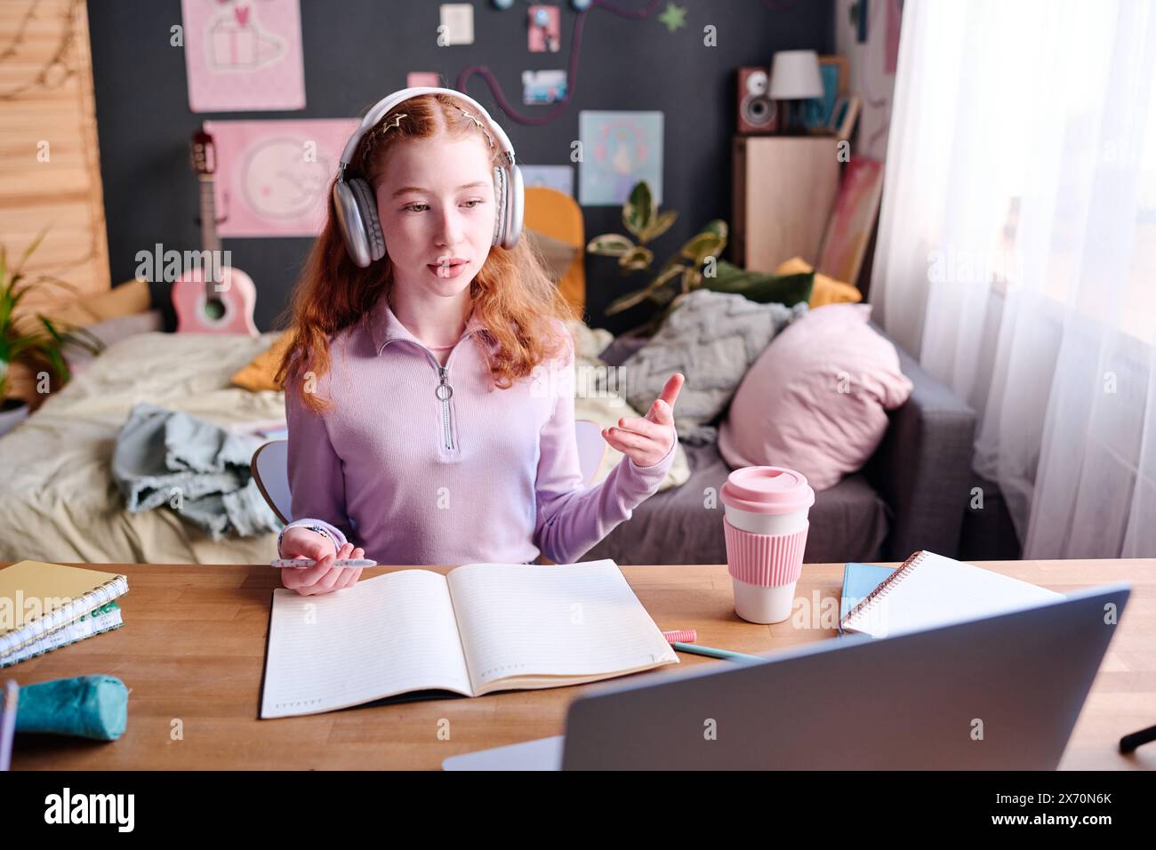 modern-teen-schoolgirl-wearing-headphones-sitting-at-desk-in-her-room