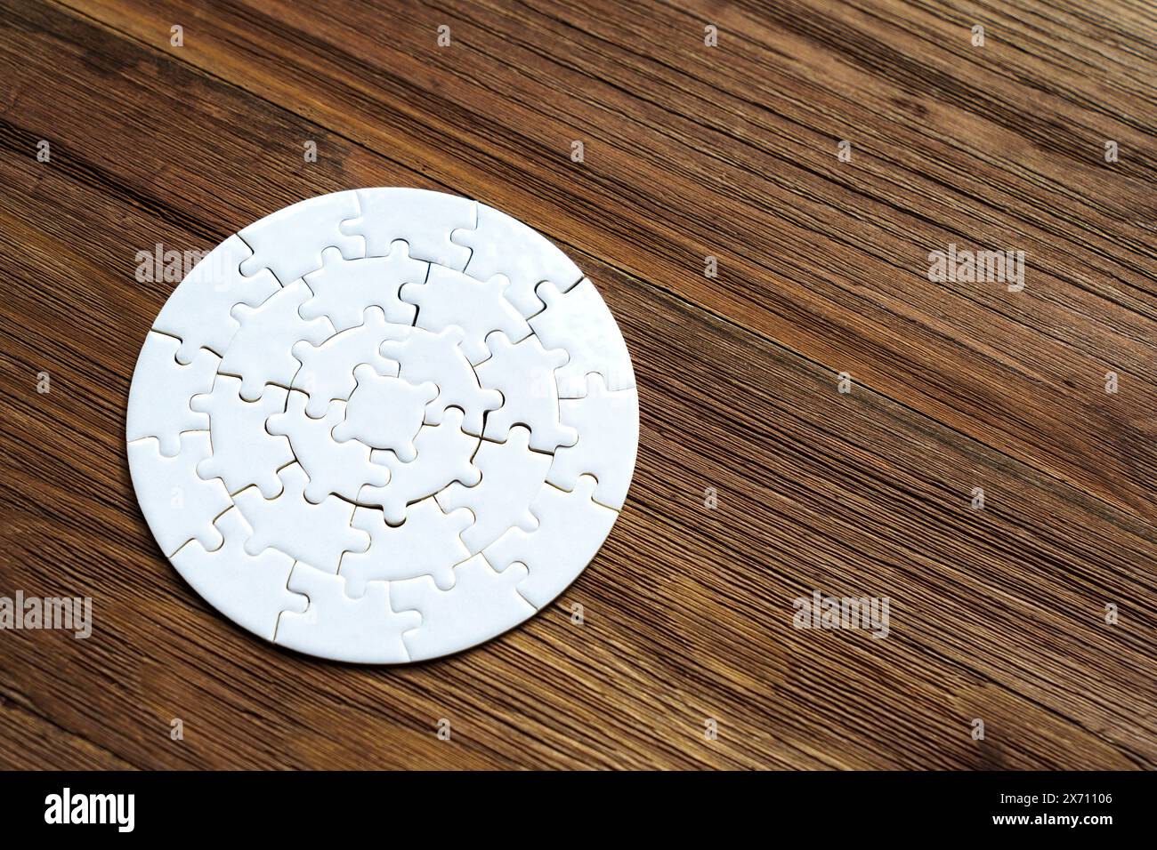 Close-up of a white circular jigsaw puzzle set on a wooden background with copy space. Creative time related concept. Stock Photo