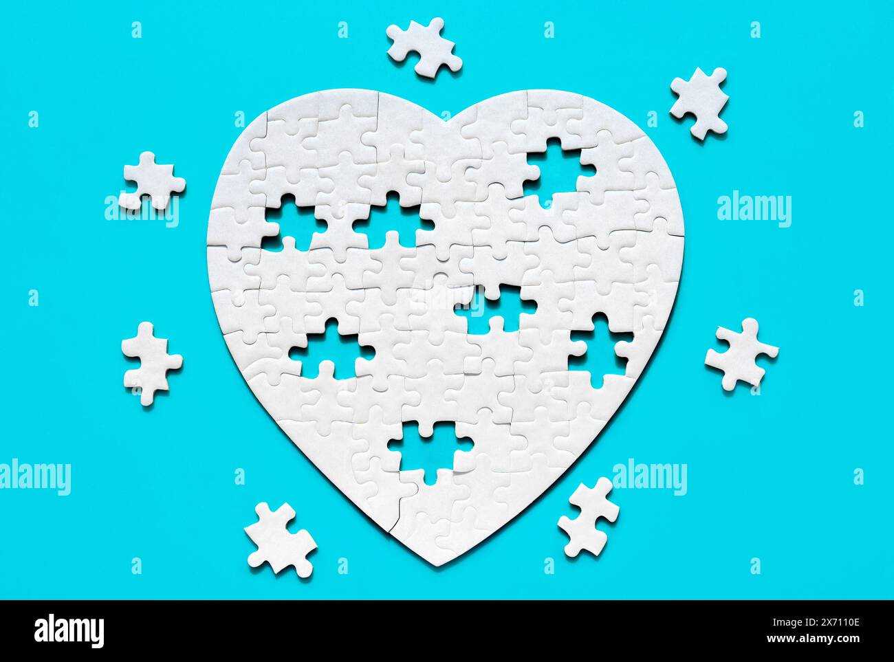 Incomplete white heart-shaped jigsaw puzzle and missing pieces arranged on a serene blue backdrop. Love and unity related concept. Stock Photo