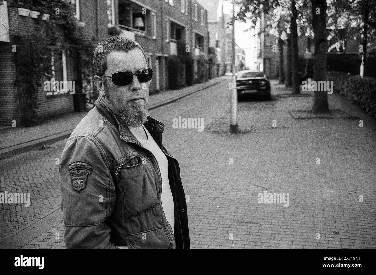 Portrait Man in Street Mature adult man wearing sunglasses roaming the streets of Dwaalgebied, a down town neighbourhood with history. Image Shot on Analog Black & White Film. Tilburg, Netherlands. MRYES Tilburg Langestraat Noord-Brabant Nederland Copyright: xGuidoxKoppesxPhotox Stock Photo