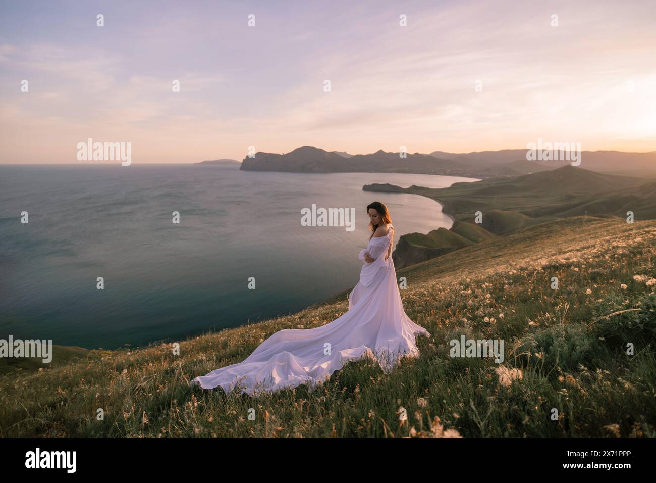 A woman in a white dress stands on a hill overlooking the ocean Stock ...