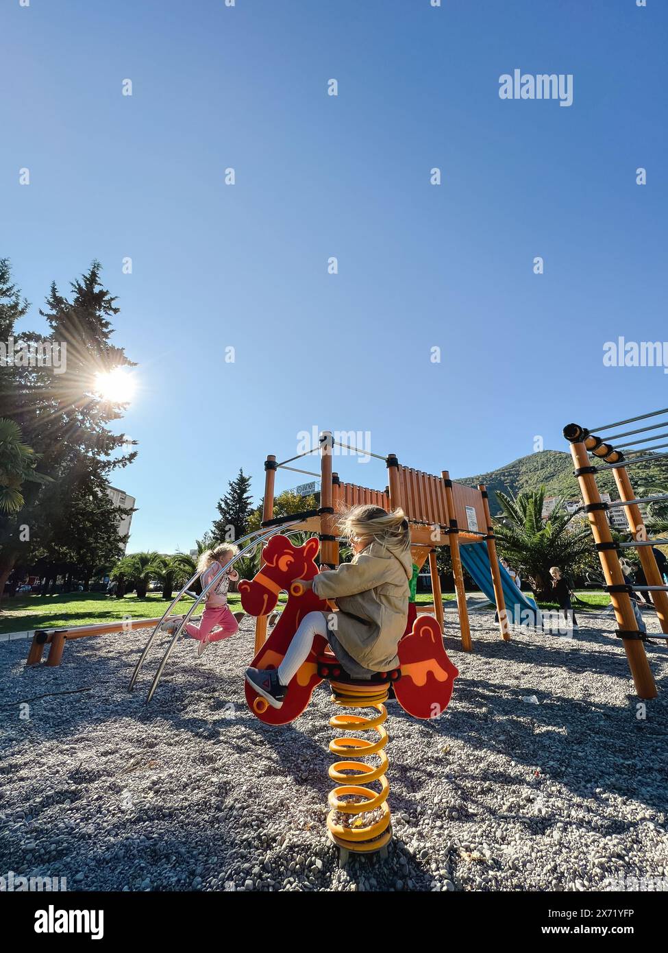 Little girl swings on a spring-swing with her hair blowing in the wind ...