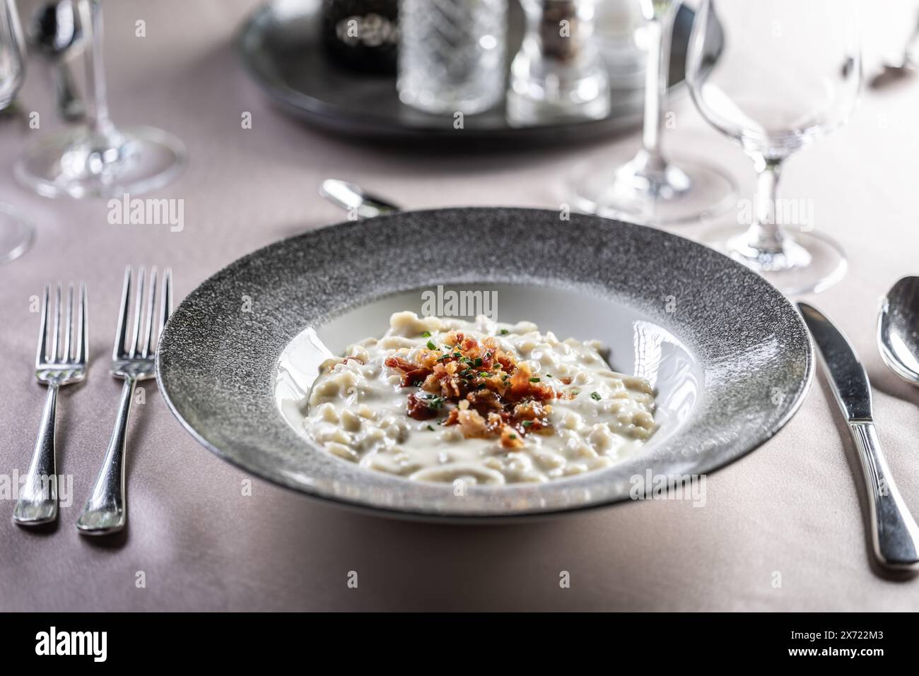 Halusky as traditional Slovak potato gnocchi with sheep cheese bryndza, fried bacon and chives served in a modern plate and on a festively laid restau Stock Photo