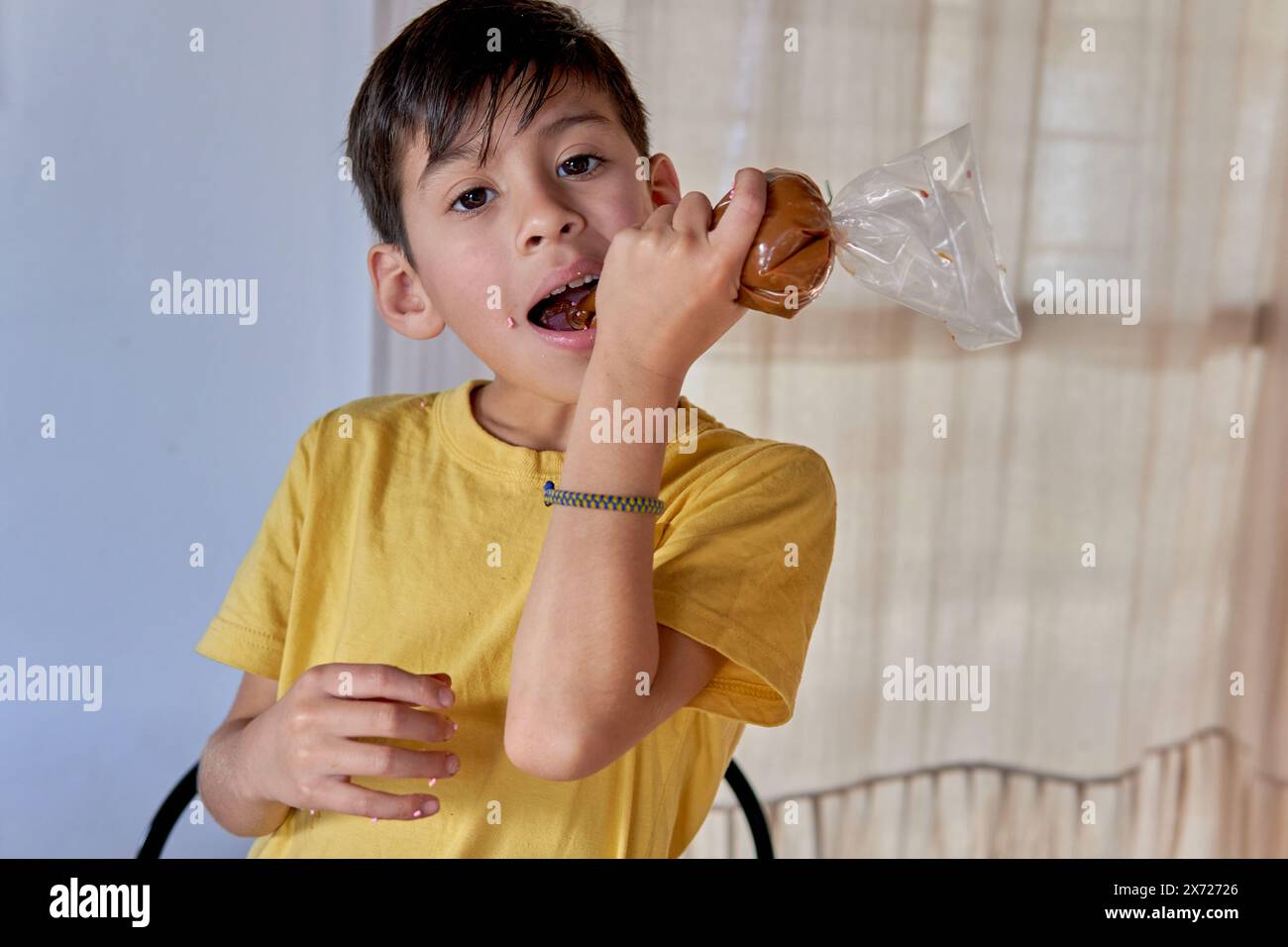 Latin boy looking at the camera eating dulce de leche from a sleeve