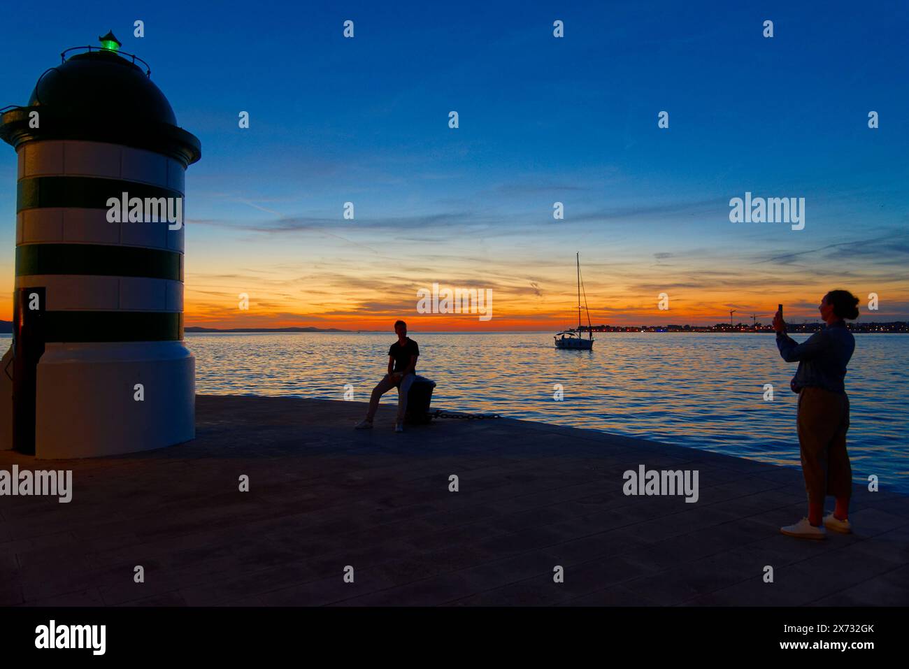 le phare à la sortie du port de Zadar en croatie au coucher du soleil et des amoureux qui se prennent en photo Stock Photo
