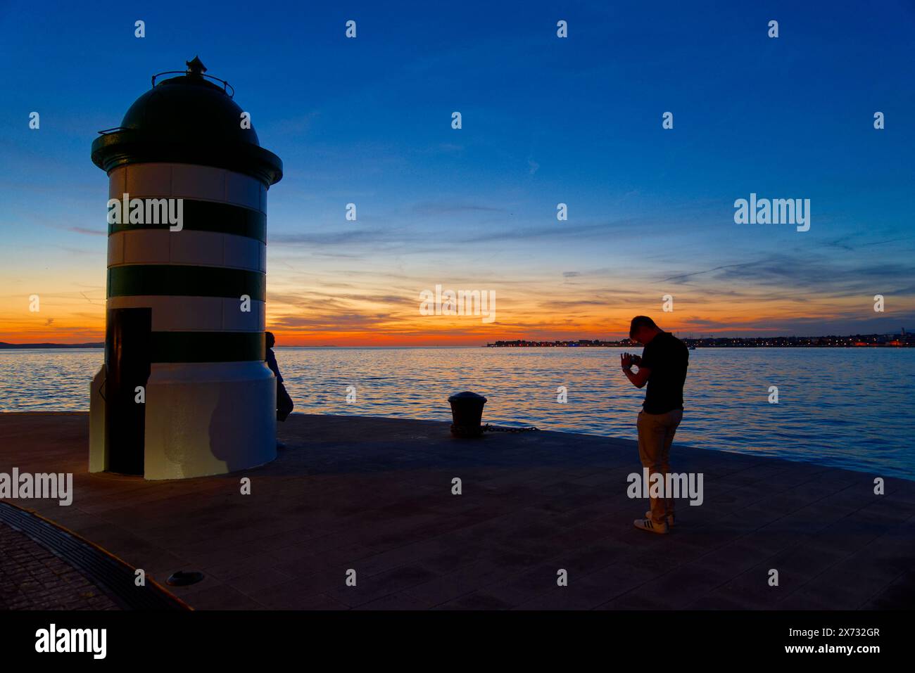 le phare à la sortie du port de Zadar en croatie au coucher du soleil et des amoureux qui se prennent en photo Stock Photo