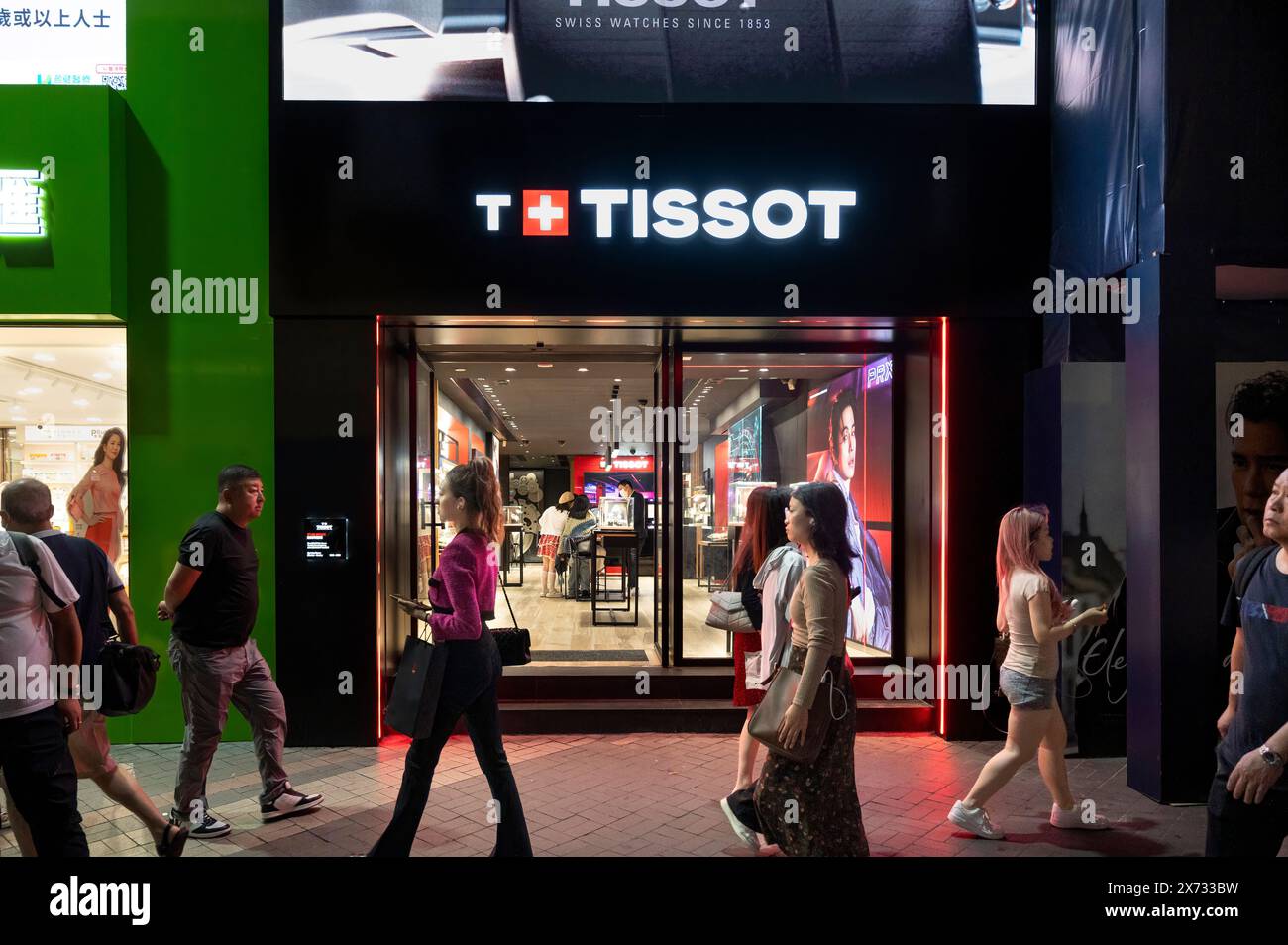 Pedestrians walk past the Swiss luxury watchmaker Tissot store seen in Hong Kong. Stock Photo