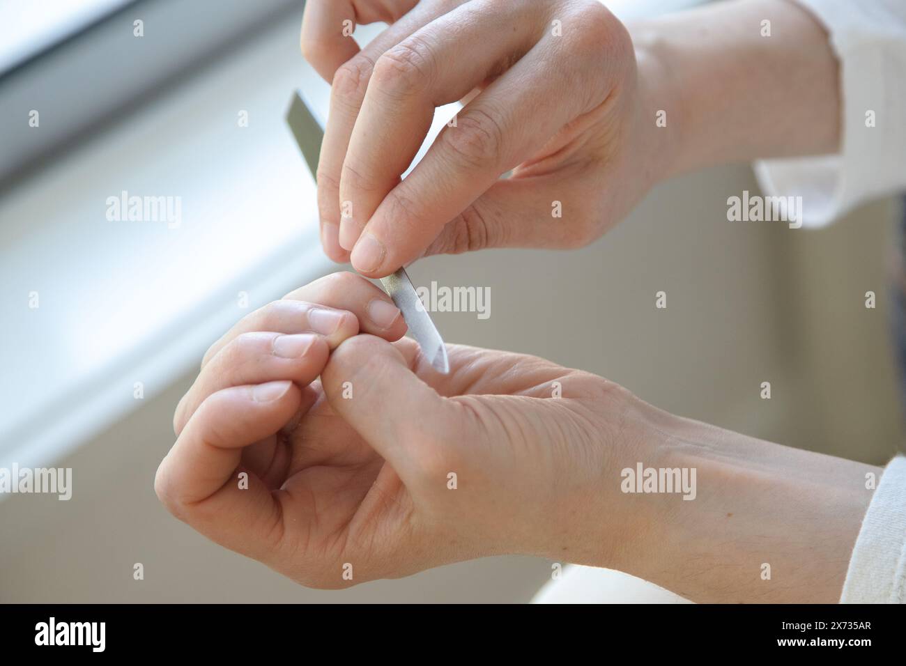 A person carefully filing their nails at home, focusing on self-care and grooming. Stock Photo