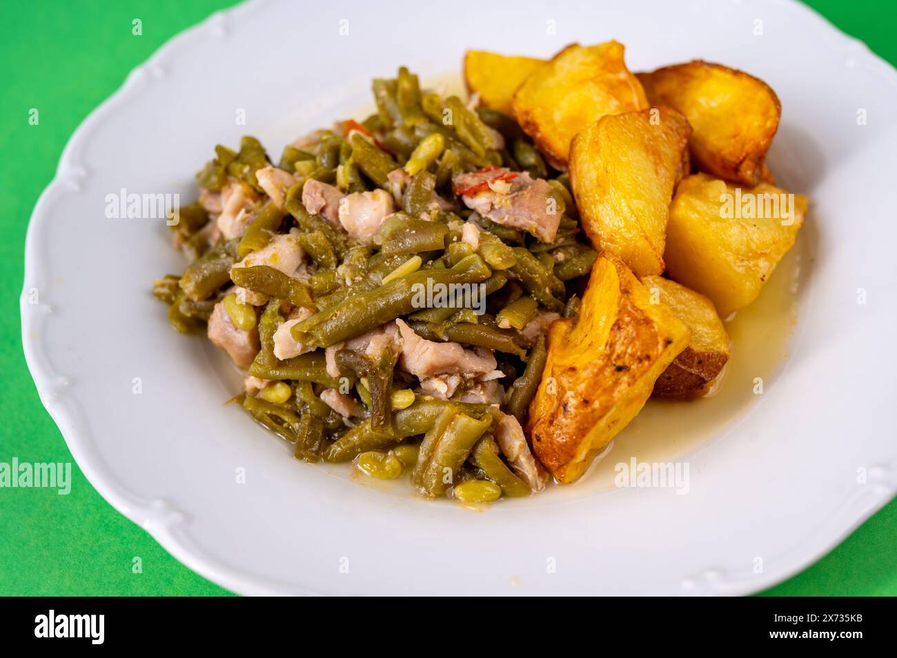 Green beans with tuna fish piece and baked potato on white plate on green background, closeup. Stock Photo