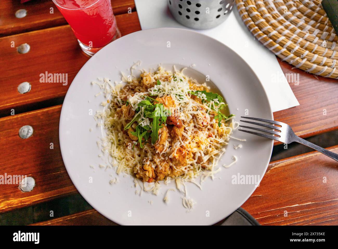 Risotto with piece of chicken meat with curcuma, grated cheese and rucola leaf on white plate, fork on restaurant table. Stock Photo