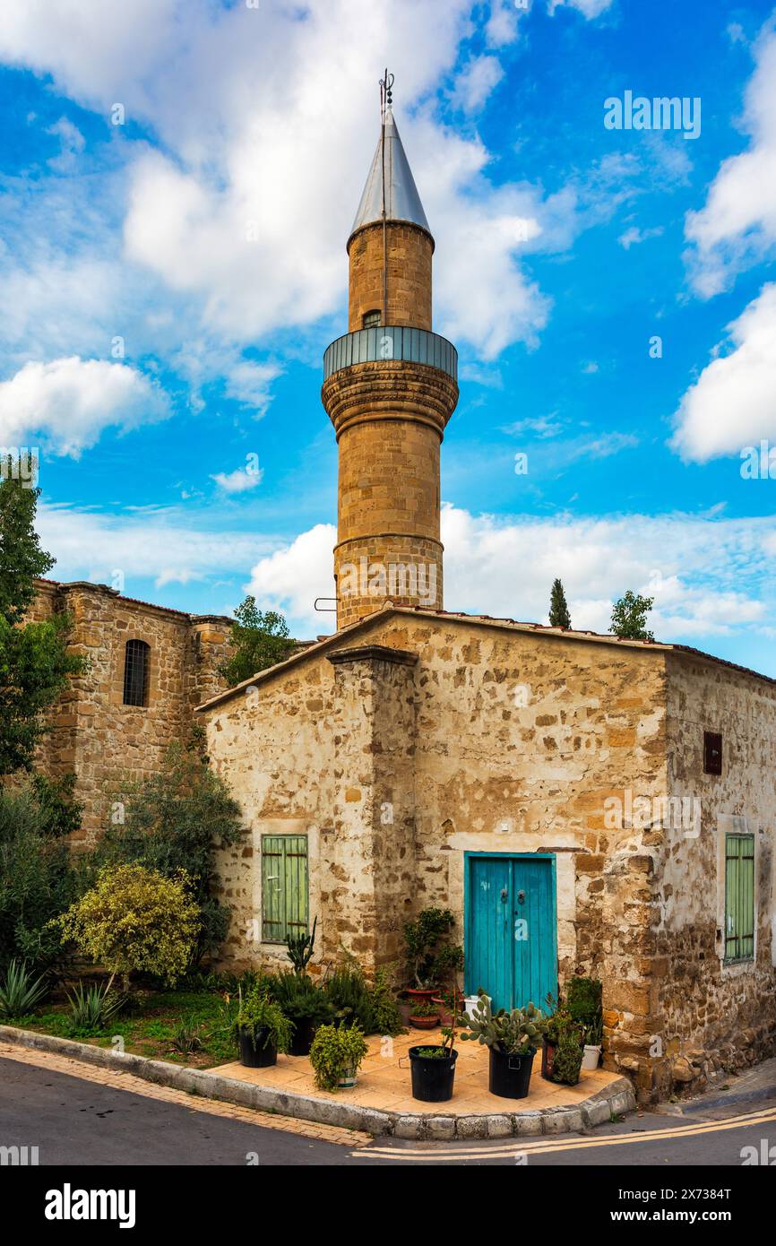 A small building with a blue door sits in front of a large Mosque with a tall tower in Nicosia, Cyprus. Beautiful street with old architecture in Nico Stock Photo