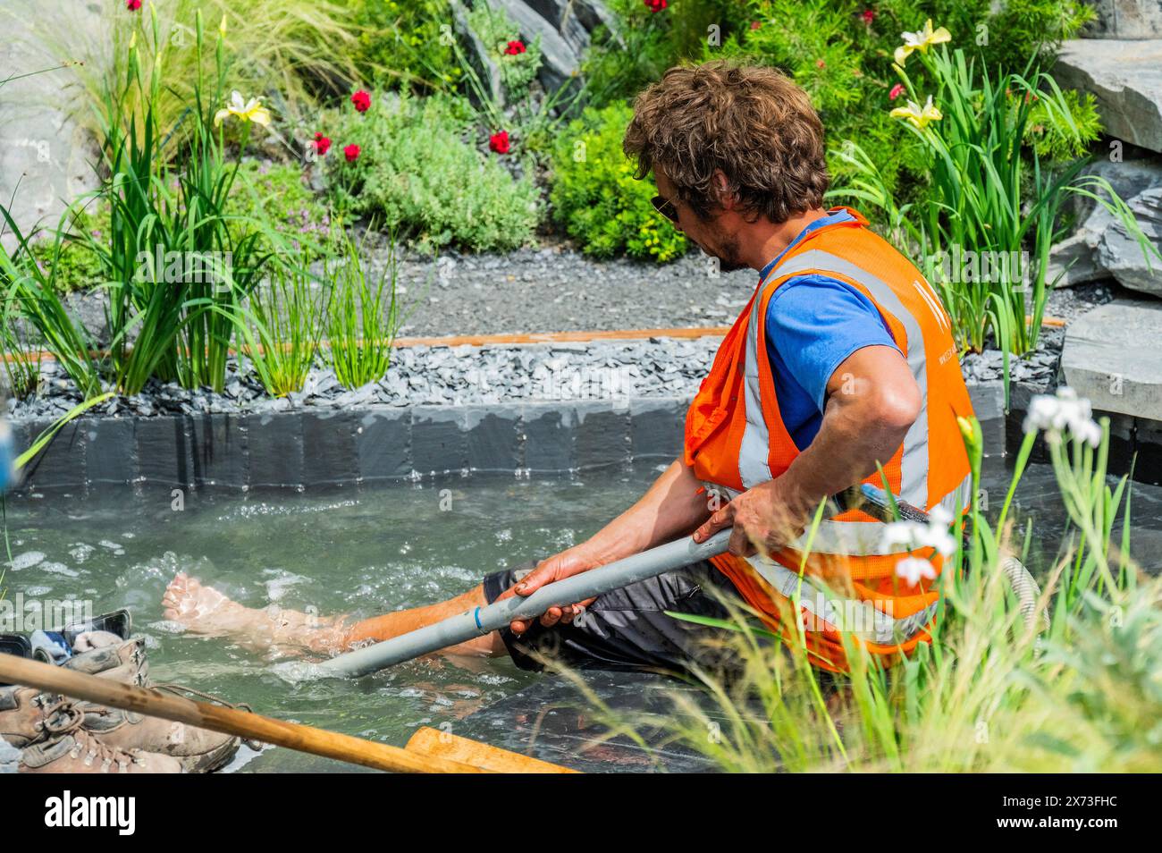 London, UK. 17th May, 2024. It is hot weather and the pond expert enjoys cooling his feet off in one of teh pools - Final preparations for the Terrence Higgins Trust Bridge to 2030 Show Garden, Designed by Matthew Childs, Built by Yoreland Design Ltd - The RHS Chelsea Flower Show 2024. It runs from 20-25 May. Credit: Guy Bell/Alamy Live News Stock Photo