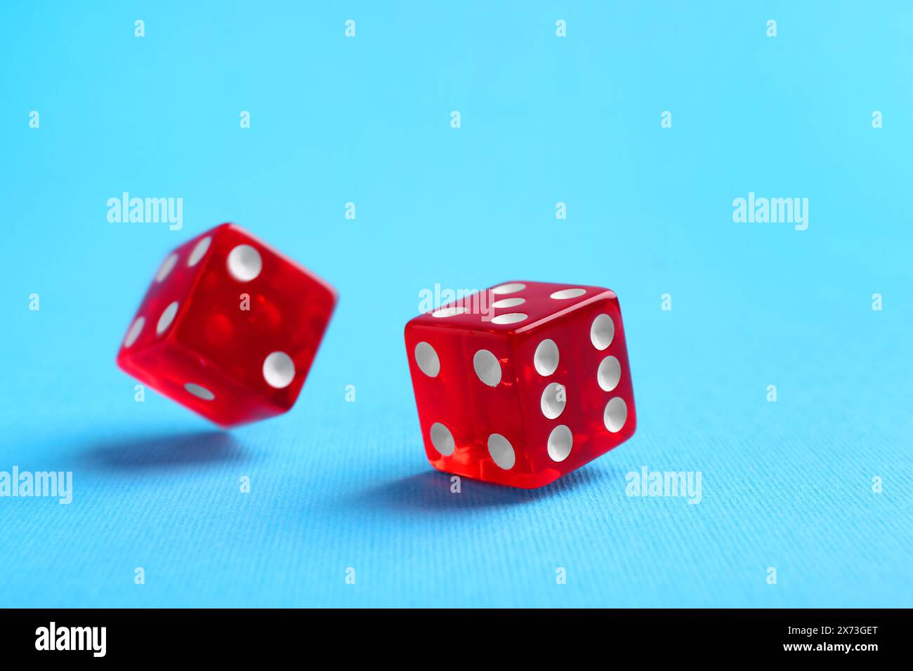 Two red game dices falling on light blue background, closeup Stock Photo