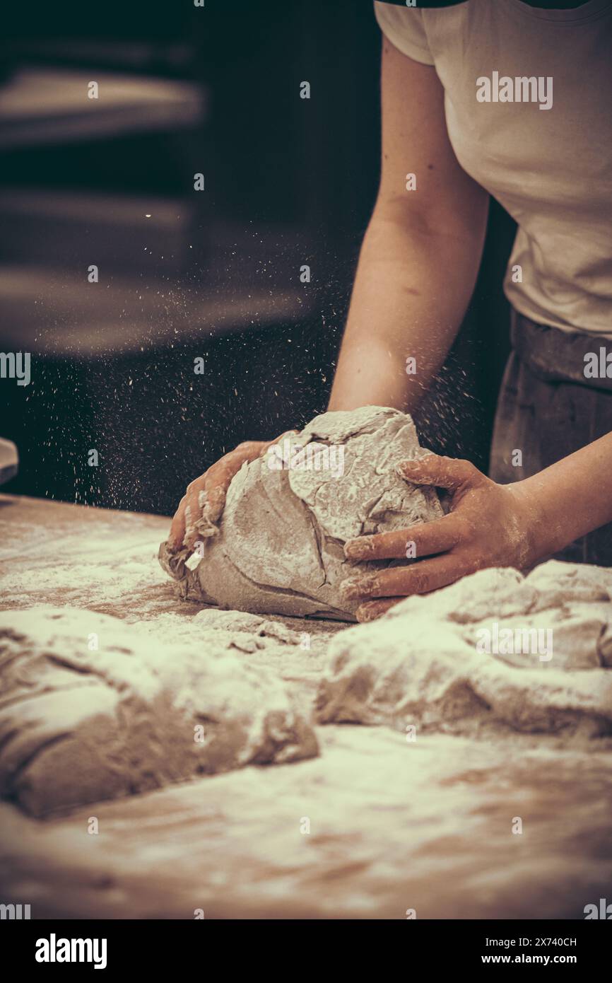 A female baker kneads bread dough in the bakery. Vintage style with grain. Vertical. Stock Photo