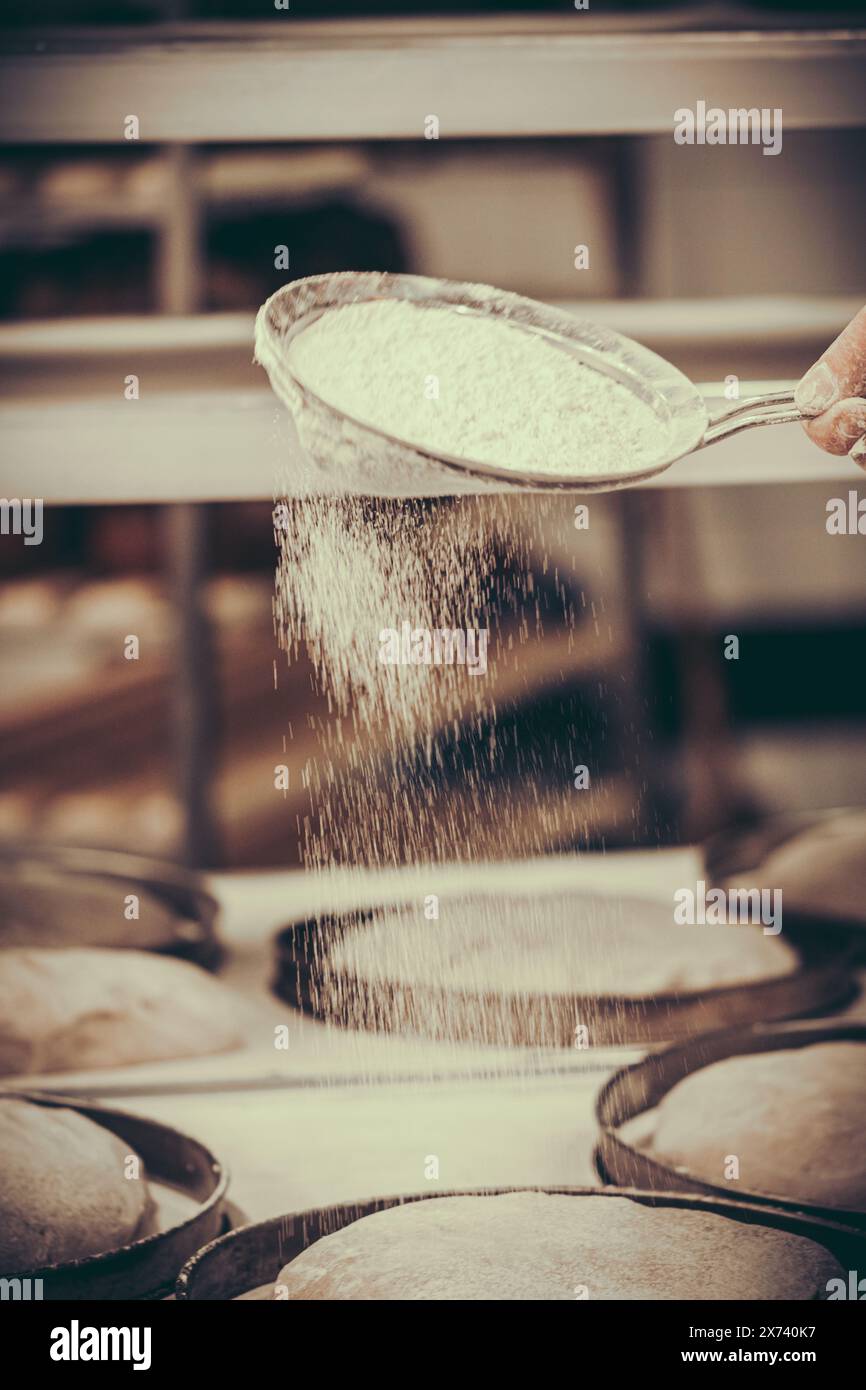 Baker's hand sifting flour over loaves of raw bread, vintage style with