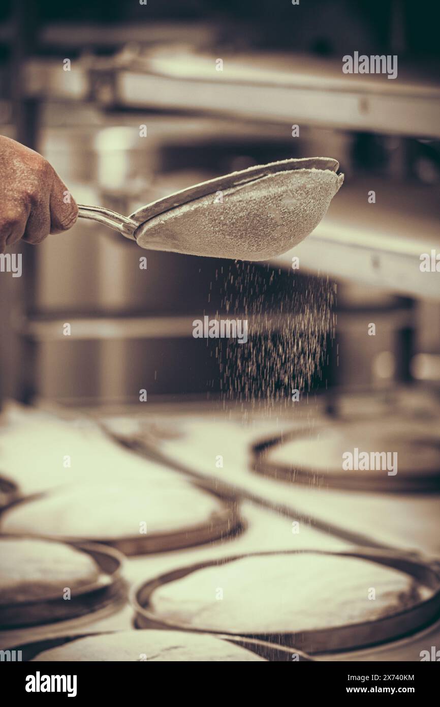 Baker's hand sifting flour over loaves of raw bread, vintage style with grain, vertical Stock Photo