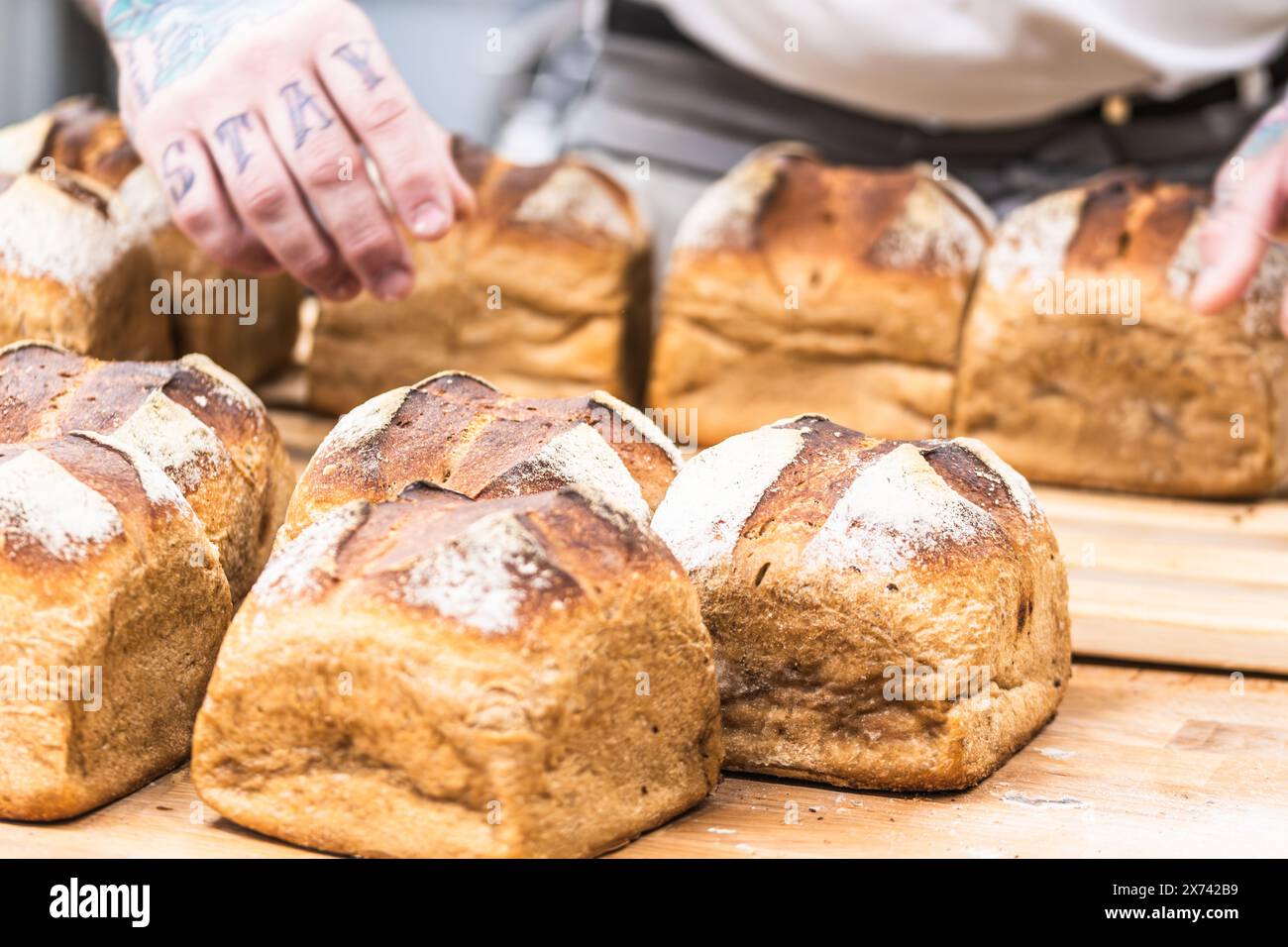 Professional baker holding wooden tray with freshly baked hot bread loaves. Stock Photo