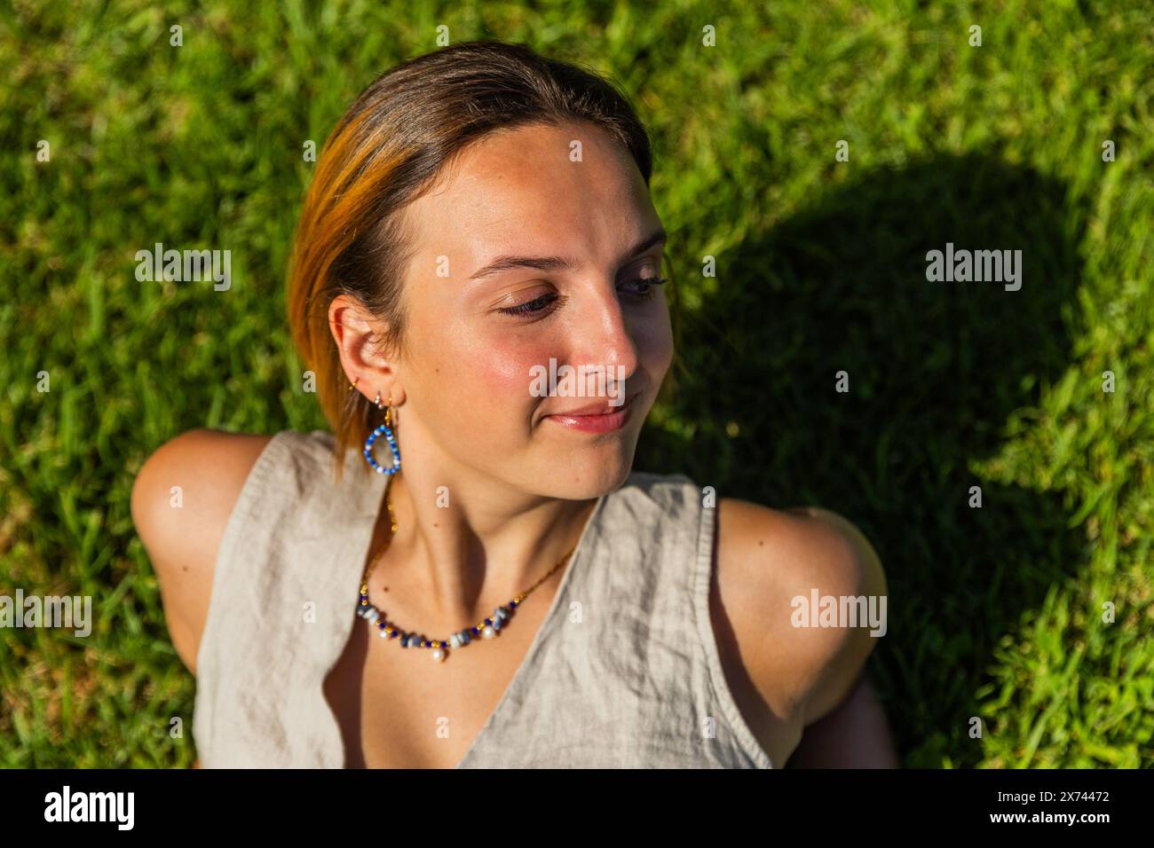 A woman is laying on the grass and wearing a necklace smiling, photo with copy space. Stock Photo