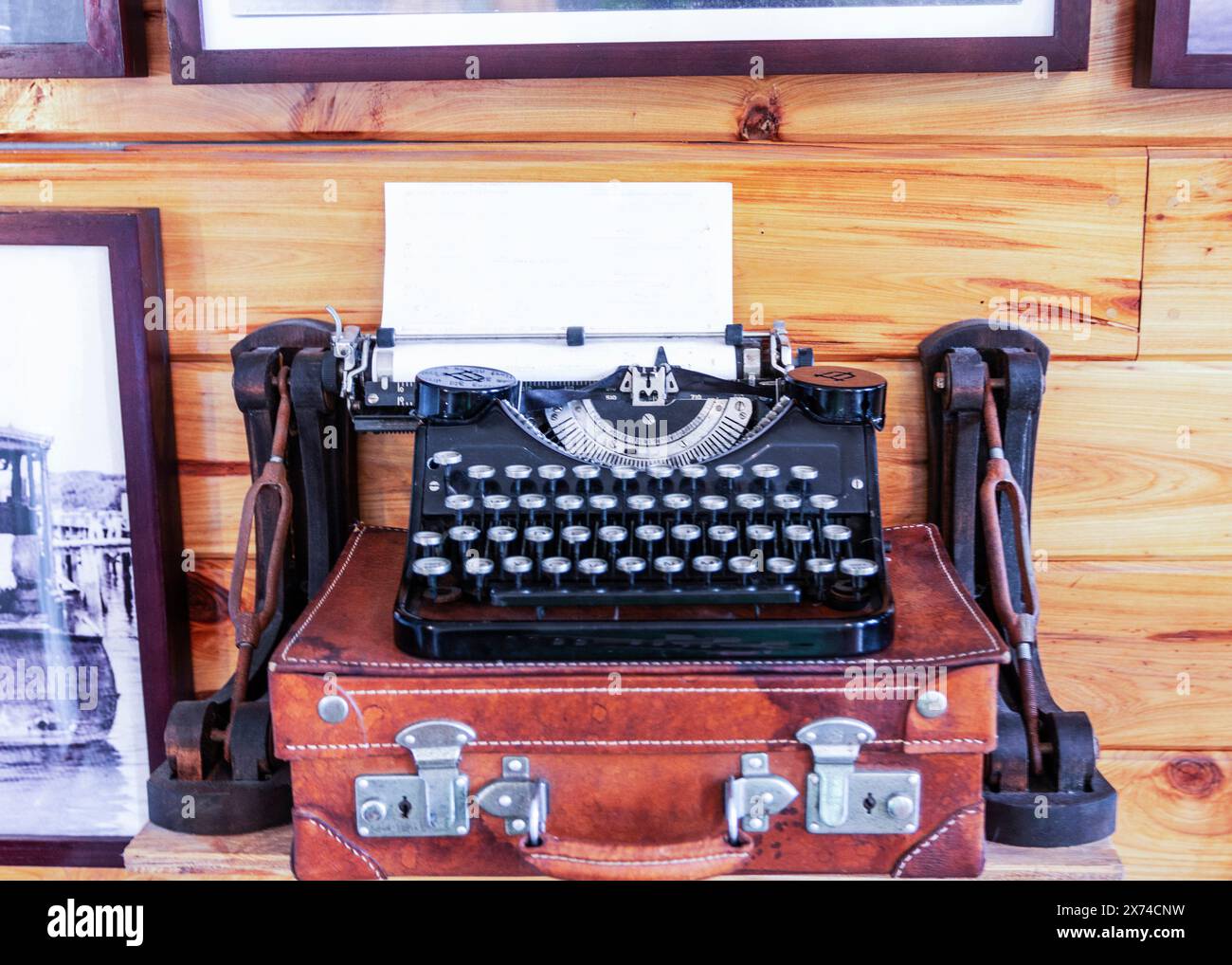 An old-fashioned typewriter is placed on top of a vintage suitcase, creating a nostalgic scene. The typewriters keys and the worn leather of the suitc Stock Photo