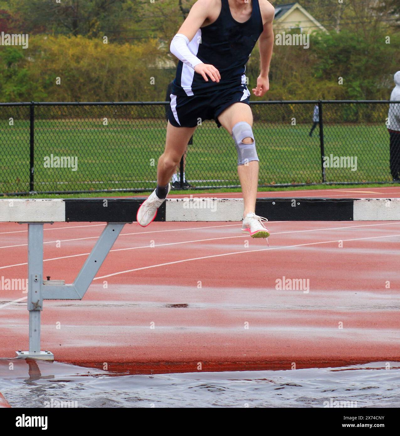 One high school boy running the steeplechase at a track meet pushing off of the barrier over the water. Stock Photo