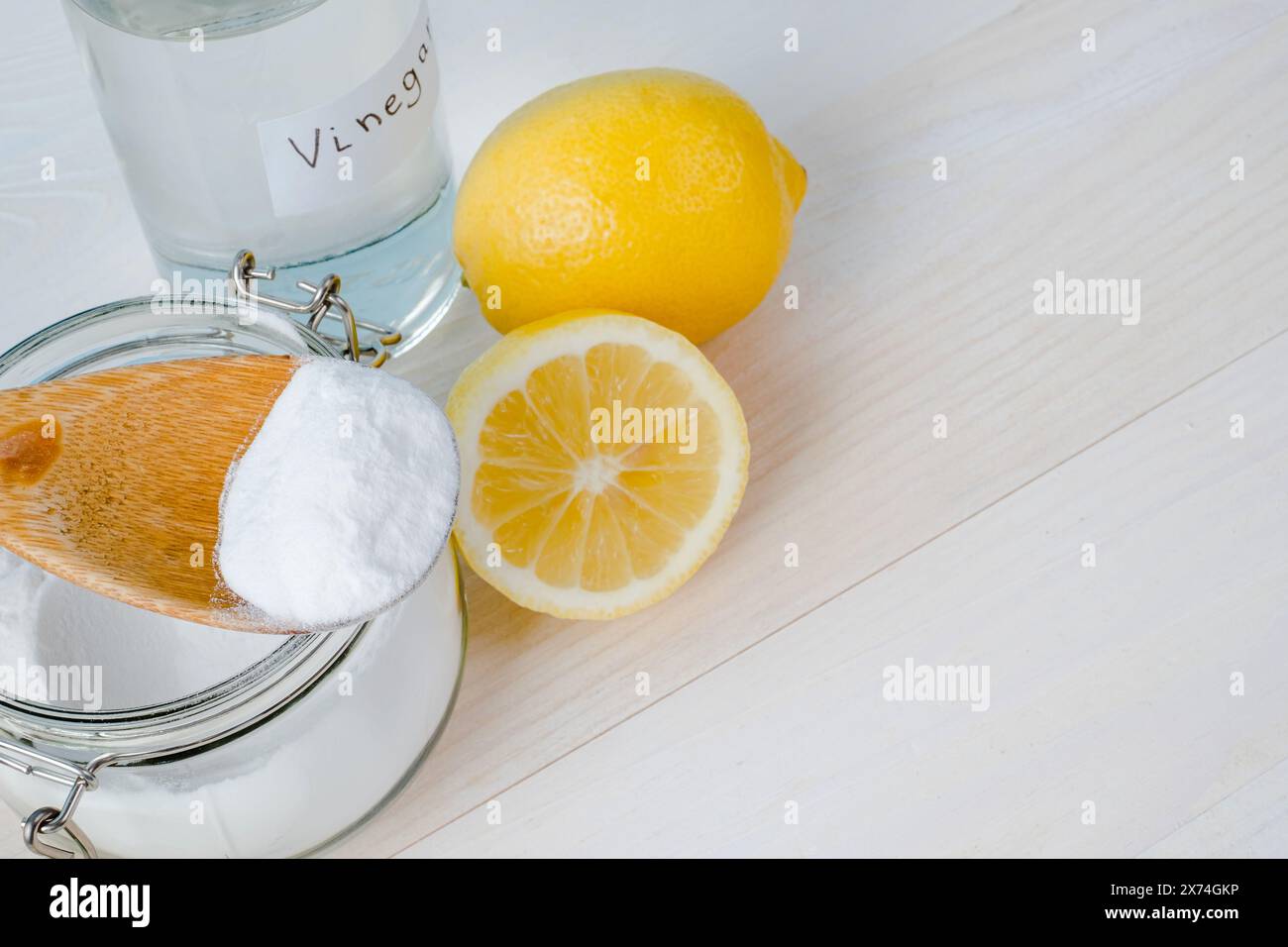 Open jar of baking soda with a wooden spoon on top, vinegar, cut lemon