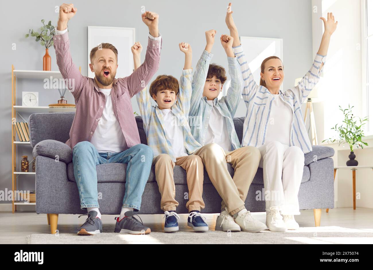 Family fans sitting on sofa and watching football match on tv rejoicing scoring goal. Stock Photo