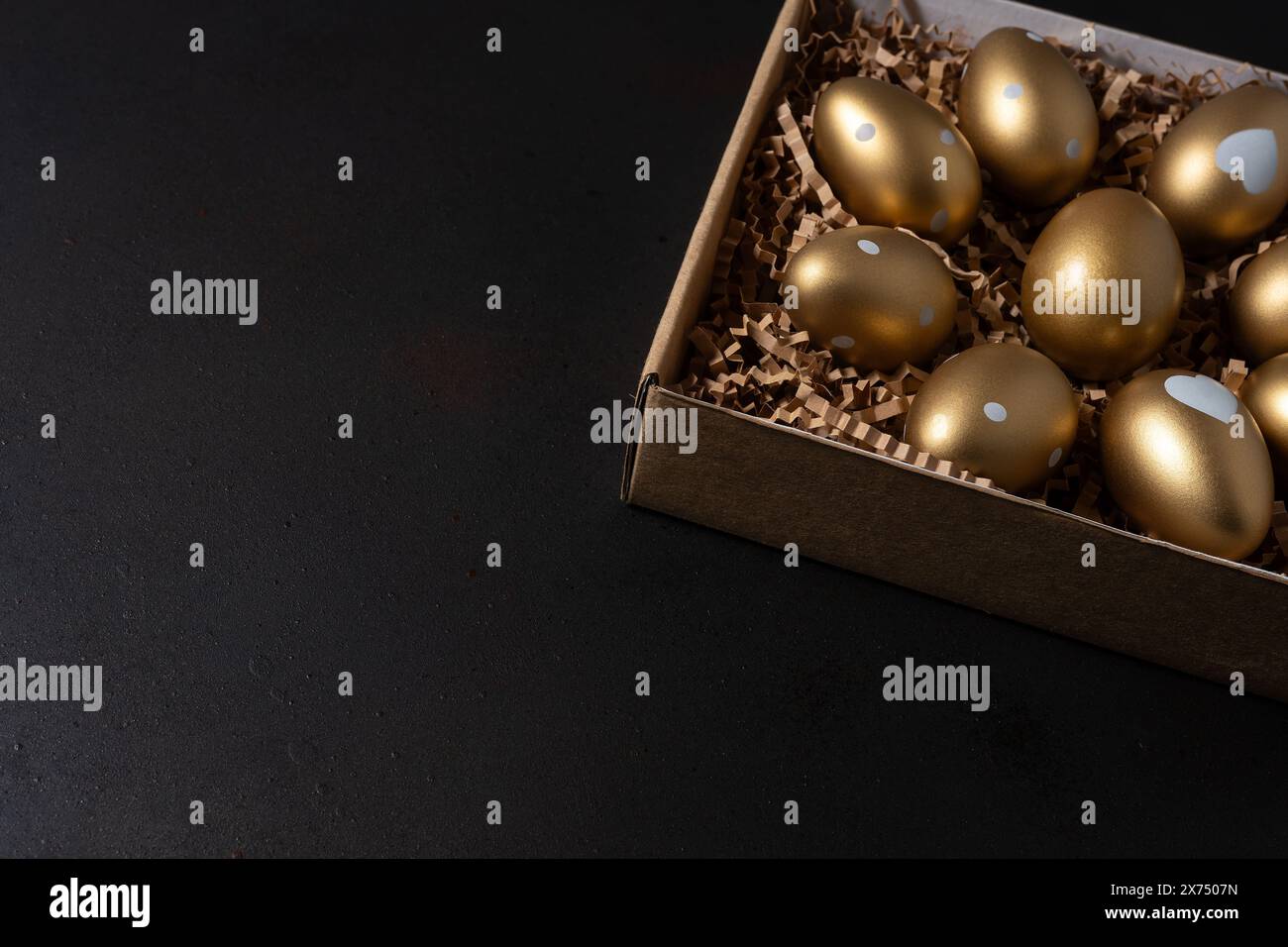Golden eggs in paper box on dark table. Stock Photo