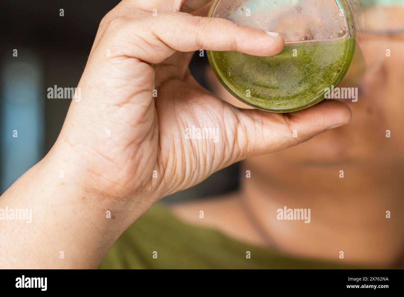 Drinking detox green vegetable juice in the morning from a glass. Hands