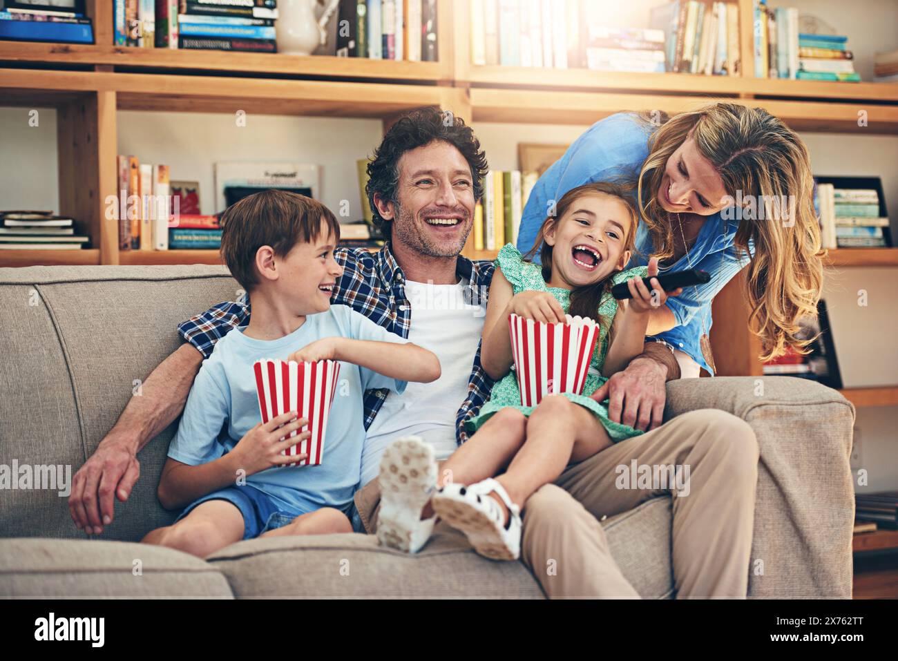 Happy family, watching tv and laughing with popcorn for funny movie, weekend or holiday on living room sofa at home. Mom, dad and young children with Stock Photo