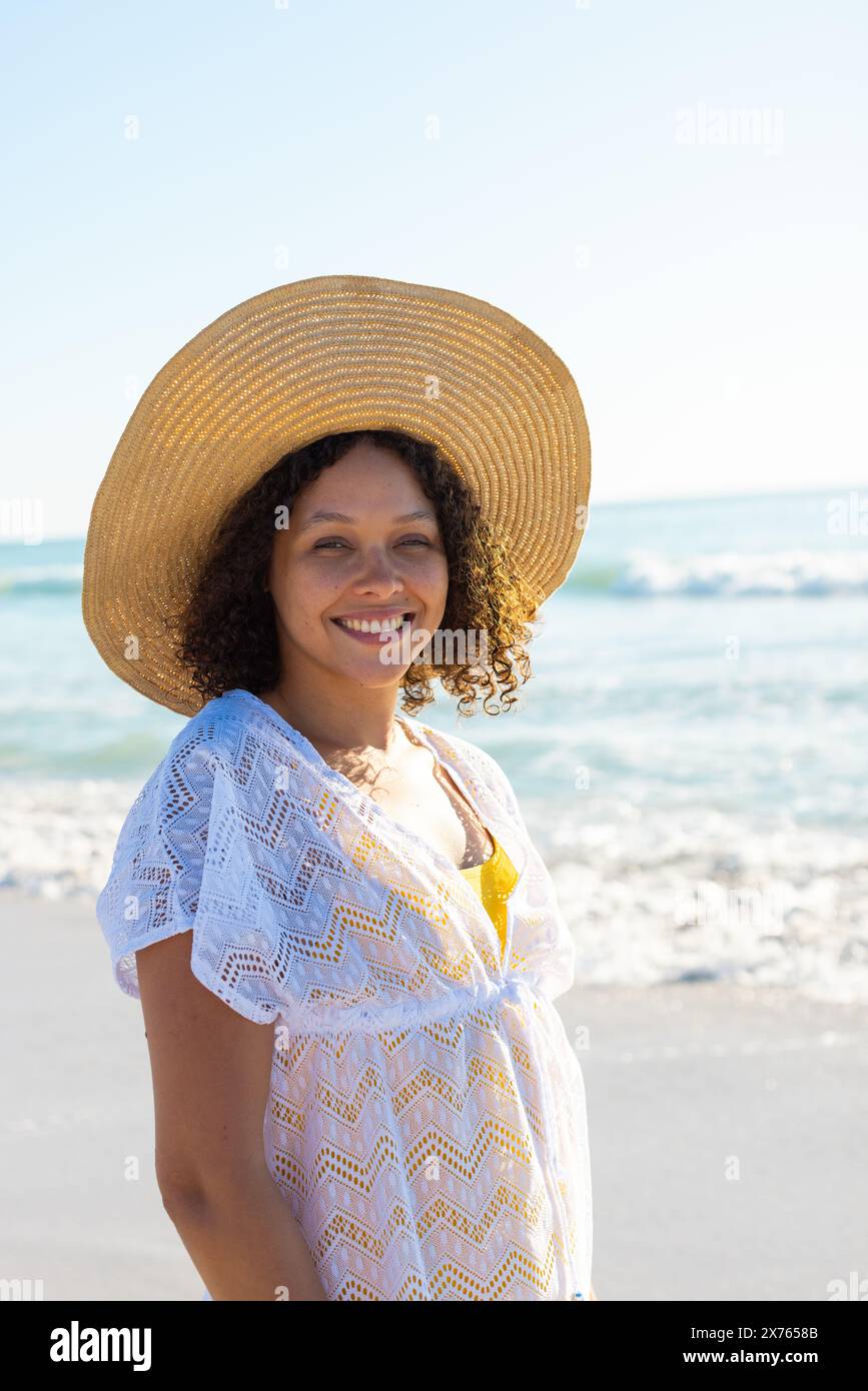 At beach, biracial young woman wearing sun hat, smiling Stock Photo
