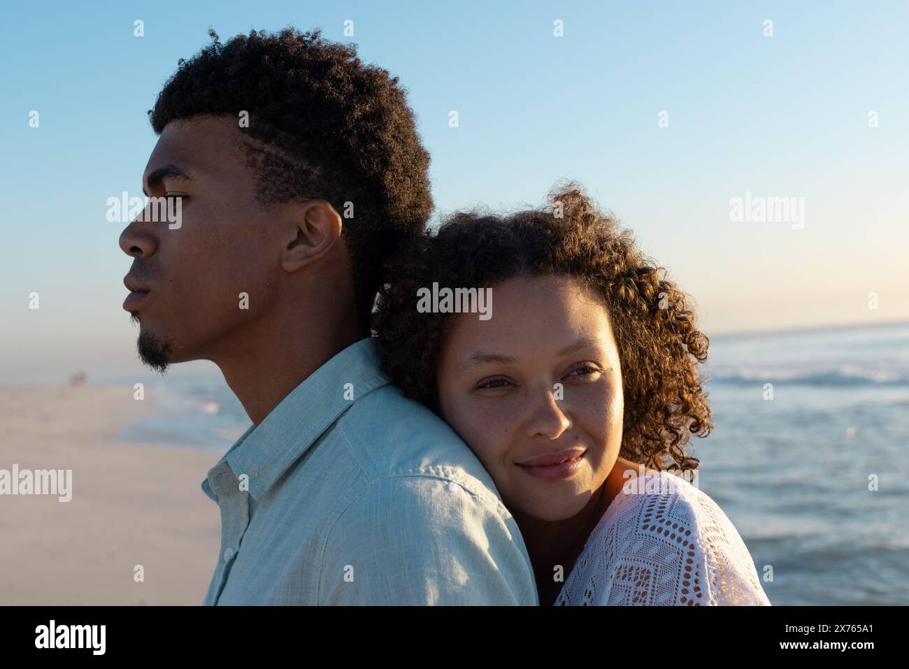 At beach, biracial couple standing, woman resting head on man's shoulder Stock Photo