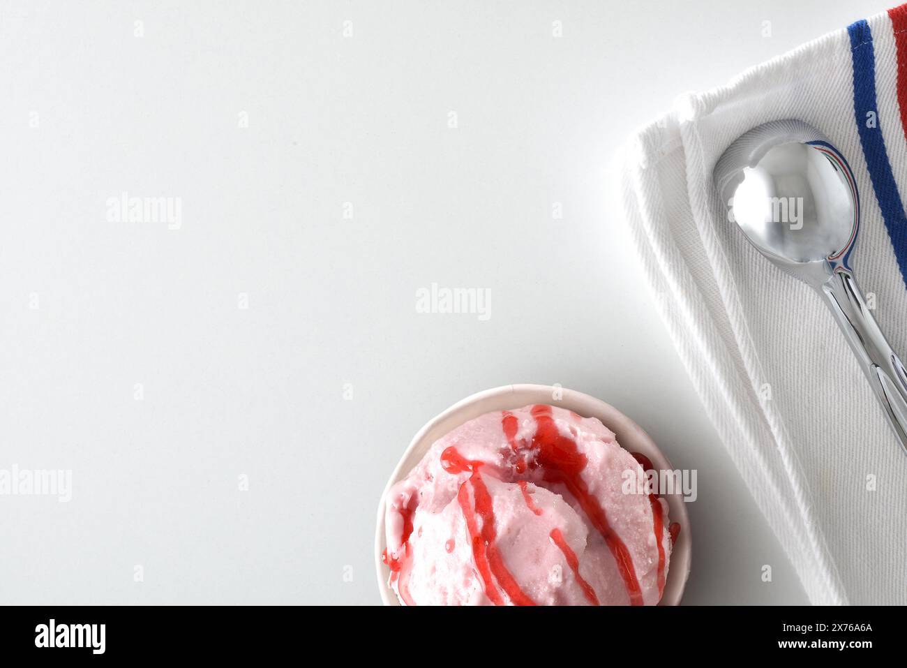 Background with paper cup with scoop of strawberry ice cream decorated with syrup on white table with napkin and spoon. Top view. Stock Photo