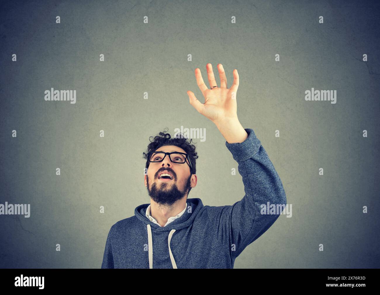 Young man with a raised up hand trying to catch something above Stock Photo