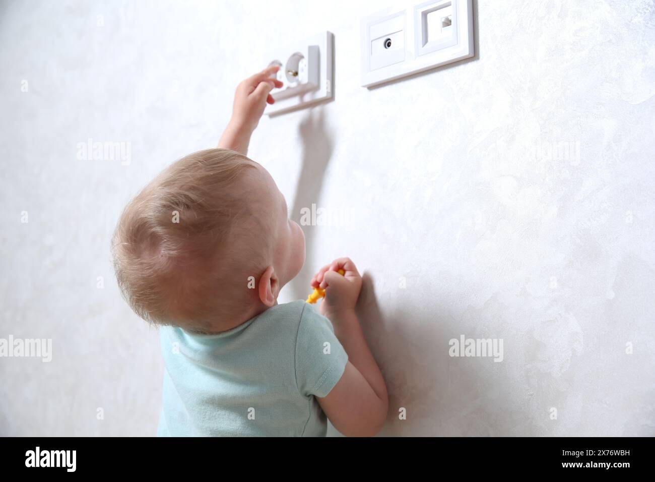 Little child playing with electrical socket indoors. Dangerous situation Stock Photo