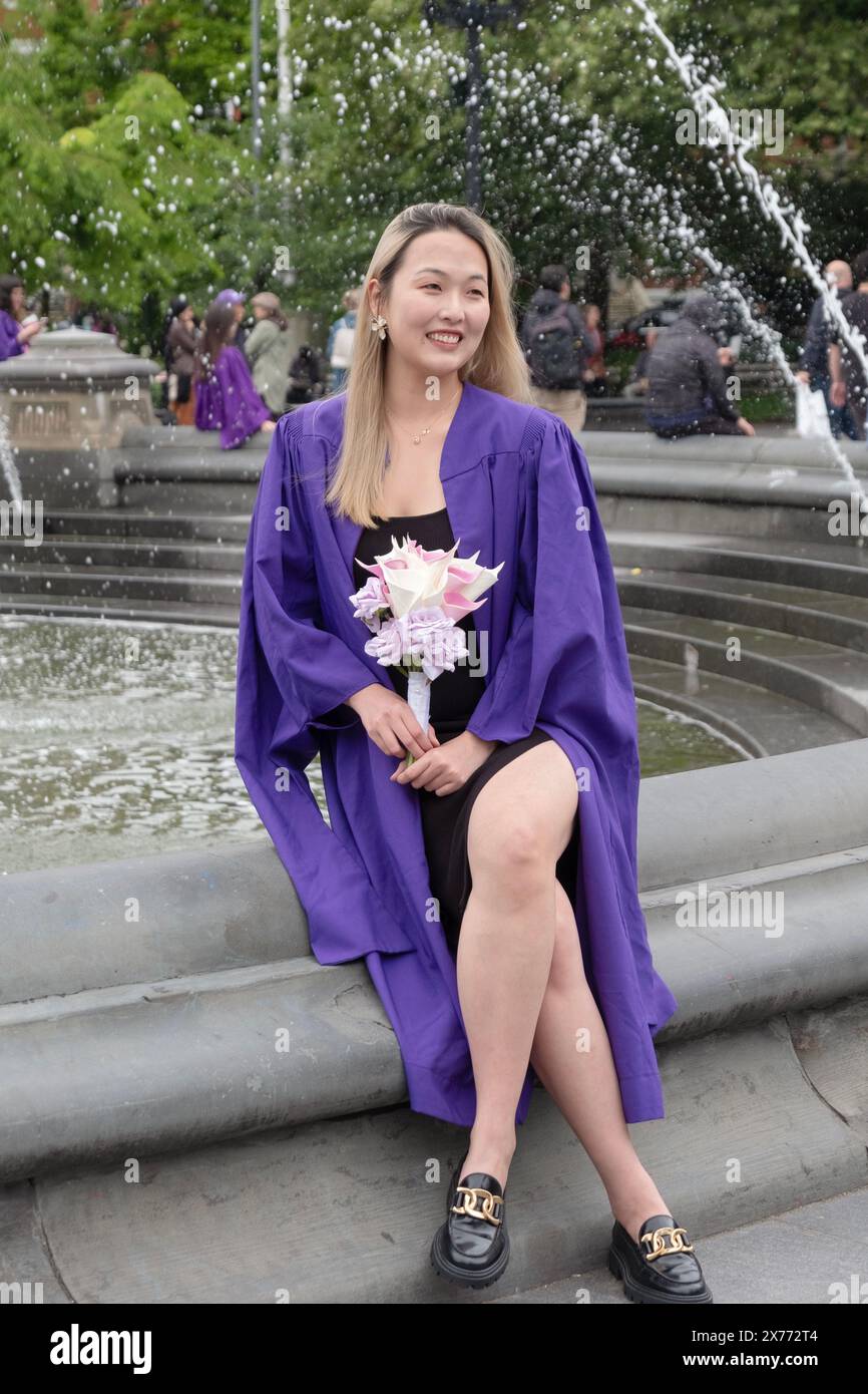 After the NYU 2024 graduation ceremony a beautiful Asian American woman poses for photos while holding flowers. In Washington Square Park in Manhattan Stock Photo