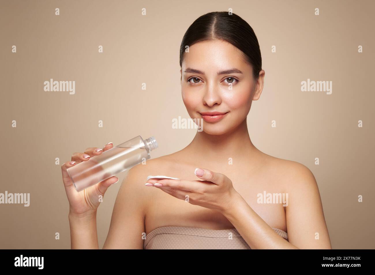 Smiling woman holds bottle with cosmetic tonic. Photo of attractive woman with perfect makeup on beige background. Beauty and skin care concept. Remov Stock Photo