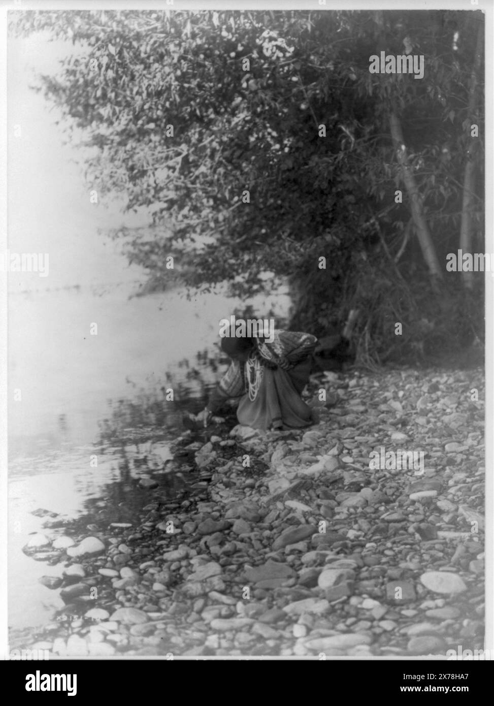 By the river Flathead, Curtis no. 3151-10., Forms part of: Edward S. Curtis Collection ., Published in: The North American Indian / Edward S. Curtis. [Seattle, Wash.] : Edward S. Curtis, 1907-30, Suppl. v. 7, pl. 236.. Indians of North America, Women, 1910. , Salish Indians, Women, 1910. , Drinking vessels, 1910. , Rocks, 1910. Stock Photo